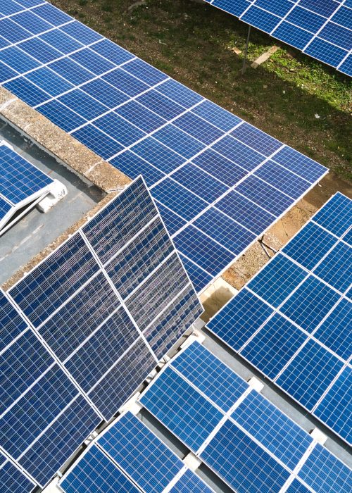 Aerial view of solar power plant with blue photovoltaic panels mounted on industrial building roof for producing green ecological electricity. Production of sustainable energy concept.